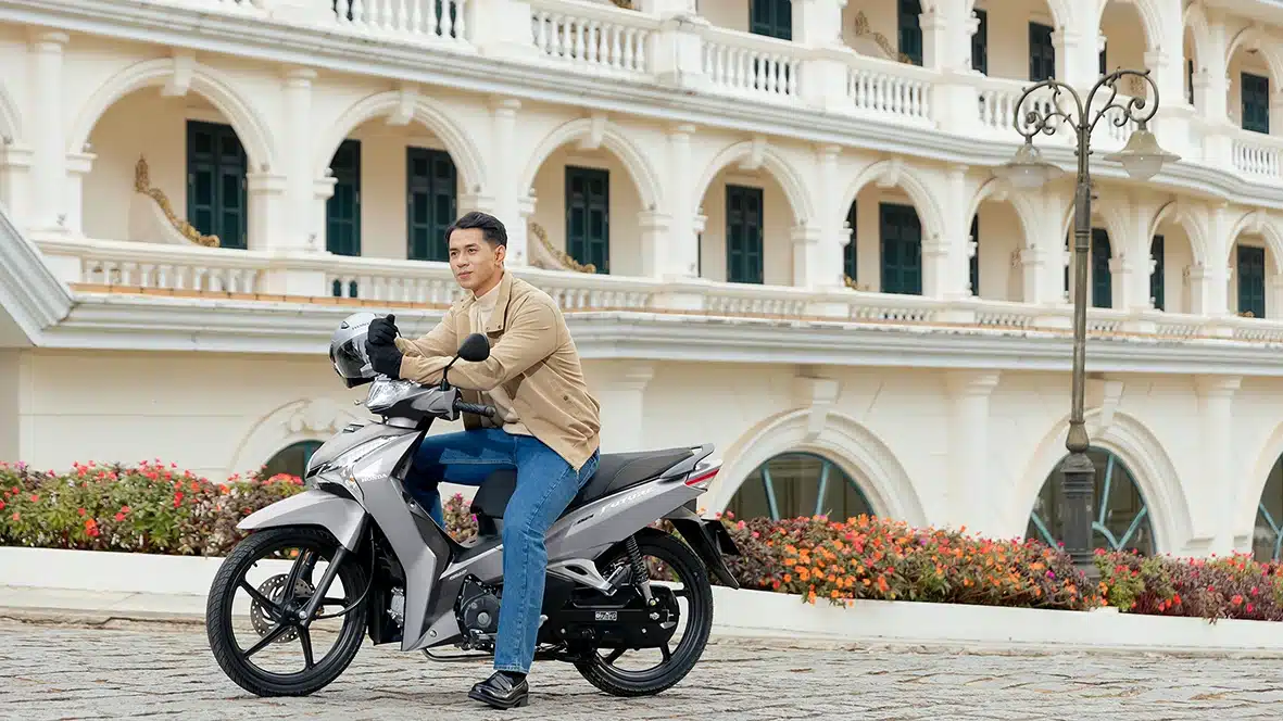 Người đàn ông lái xe Future 125 FI 2026 màu Bạc đen xám trên con đường lát đá trước tòa nhà