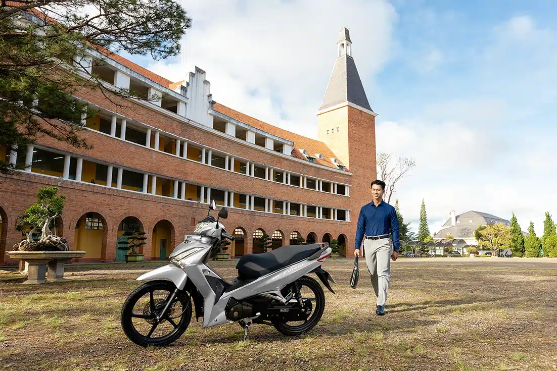 Xe Future 125 FI 2026 bản Đặc biệt màu Bạc đen xám đỗ trên bãi cỏ trước tòa nhà cổ, người đàn ông đứng bên cạnh